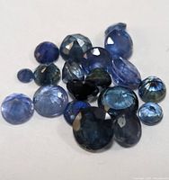 Close-up image of multiple loose blue sapphires in various cuts and sizes spread on white background.