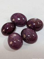 Five polished oval cabochon star rubies with visible asterism and some natural inclusions, shown on white background.