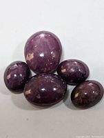Five genuine star ruby cabochons laid out on a plain white background, showing their size, shape, and surface details.