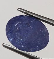 Close-up image of oval shaped genuine tanzanite gemstone, showing violet-blue coloration and visible internal inclusions.