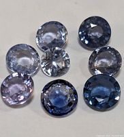Nine round faceted tanzanite gemstones in various light to deep blue violets shades on white background.