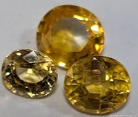 Three faceted yellow sapphire gemstones laid out, showing size and color variations.