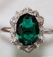Close-up front view of silver ring with green oval faceted gemstone in ornate silver setting.