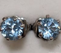 Close-up of two sterling silver stud earrings with round faceted light blue stones held by six prongs.