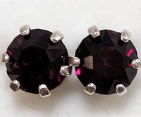 Close-up front view of two round garnet stones set in sterling silver prong settings forming a pair of stud earrings.