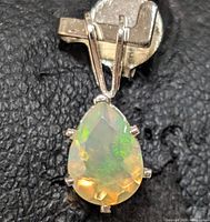 Close-up image of the opal pendant showing the teardrop-shaped faceted stone with visible green and orange opal play-of-color in a six-prong silver setting.
