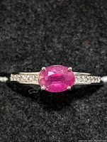 Close-up photo of the sterling silver ring showing the oval ruby center stone and accent stones on the band.