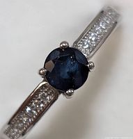 Close-up front view of sapphire center stone and cubic zirconia accents on sterling silver band.