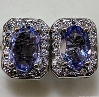Close-up front view of a pair of stud earrings featuring oval tanzanite stones with diamond halos set in sterling silver.