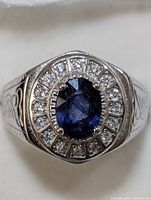 Front view of men's sterling silver ring featuring an oval blue sapphire surrounded by cubic zirconia stones.