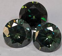 Close-up photo of three round cut gemstones with a greenish-blue tint and high brilliance.