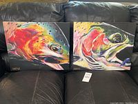 Front view of both paintings side by side on a black leather surface.
