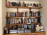 Three photos showing books and magazines on wooden shelves from different angles. The images show a large number of books in varying sizes and colors along with magazines stacked on a lower shelf.