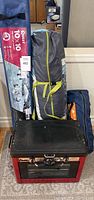 Lot contents showing a blue carrying bag for 10x10 pop-up tent, gray tent bag with yellow straps, and red Camp Chef stove oven on carpet.