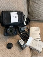 Overall view of camera bundle on couch showing camera bag, SX60 HS camera, action camera, charger, batteries and manual