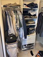 Section of closet showing hanging dress and casual shirts; garment bag at floor; black bag on shelf