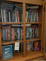 Front view of wooden cabinet filled with DVDs, showing variety of movie and music DVDs including 'Bullitt' and Neil Young titles