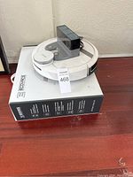 White Ecovacs Robotics robot vacuum cleaner on top of the Ecovacs product box next to the wall on a wooden floor with a MaxSold lot number front and center.