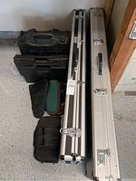 Seven empty carrying cases including soft and hard cases arranged on garage floor.