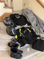 Photo of helmets, jackets, gloves, boots, and motorcycle cover arranged on stairs.
