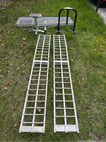 Two aluminum loading ramps laid on grass with maintenance stand and wheel chock behind