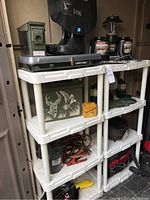Shelving unit containing various outdoor gear items including stoves, lanterns, boots, and boxes.