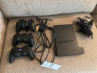 Photo of PS2 console, three controllers and cables on couch