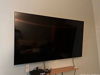 Television mounted on wall showing full front view, visible cables, small shelf beneath