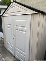 Front three-quarter view of beige Plastic Rubbermaid shed with double doors closed