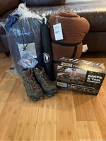 Hiking boots, two sleeping bags, trekking poles, and knife/tool sharpener in original packaging on floor.