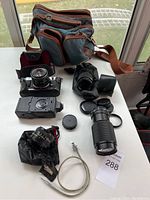 Full view capturing two vintage Canon cameras on the table with various lenses, caps, cable release, and a carrying bag.