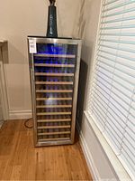 Front view of stainless steel wine refrigerator with glass door showing interior wooden shelves and auction label