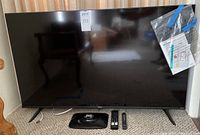 Front view of TV on its stand with two remotes and packing slip taped to screen