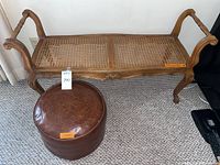 Photo of the vintage wooden cane seat bench alongside the round embossed vinyl footrest pouf on carpeted floor