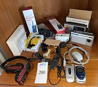 Electronics lot overview showing various boxed radios, clipped on sports radio with headphones, two flip phones, adapters, and vintage headphone set.