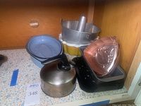 Vintage bakeware and cookware items including pans, roasting pan, kettle, molds shown inside a cabinet.