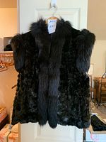 Full view of black mink fur vest showing long fur trim on neck and sleeves, checkerboard patterned body fur, displayed on a hanger.