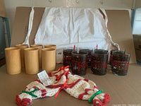 Wide shot showing seven stained glass style glass tumblers, six bamboo cups, and vintage white apron and bloomers with Christmas crocheted trim.