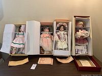 Four Victorian style porcelain dolls displayed in original boxes on table with certificates of authenticity shown in front