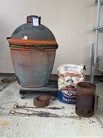 Orange Imperial Kamado BBQ smoker with extra top and accompanying items including Kingsford briquettes and a rusty chimney starter. Items shown on concrete floor.