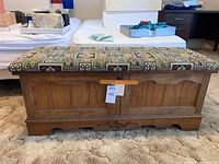 Full front view of the cedar chest showing embroidered padded top and wood panel body.