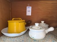 Yellow Dansk Kobenstyle saucepan with lid and white Copco Denmark enameled skillet, with two ceramic chili bowls with lids decorated with floral designs.