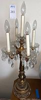 Front view of gold tone table lamp with five candle style lights and hanging crystals.