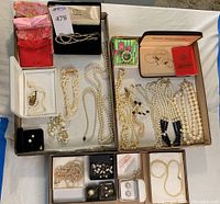 Overview of various pearl necklaces, earrings, pins, and fabric pouches laid out in trays and boxes.