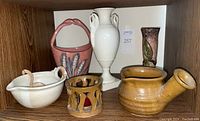 Group photo showing white Lenox vase, pink Italian ceramic basket with wheat decor, Geffer Pottery vase, brown earthenware pot with spout, handled bowl with ladle and lattice pottery piece.