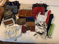 Photo of assorted purses, wallets, and umbrellas laid out on white surface showing variety of sizes, colors, and styles.