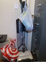 White upright Oreck vacuum with fabric bag and additional vacuum bags in a plastic Target shopping bag beside it