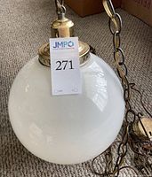 Close-up photo of milk white globe with brass cap and chain on carpet floor.