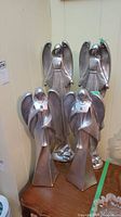 Four silver-tone angel figurines with fan-shaped wings and pyramid bases, two taller and two shorter, positioned together on a wooden surface, showing overall condition and size comparison.