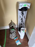 Photo showing bird feeder in box, watering can, bird house, garden figurines, and hummingbird food on the floor.